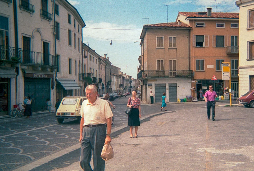 People walking across an Italian square between colourful buildings in afternoon light.